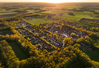 Luftfoto af et glampingområde omgivet af skov og marker under solnedgang, perfekt til naturophold.