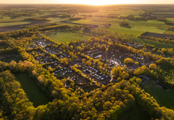 Vista aerea di un glamping immerso nei boschi e campi al tramonto, ideale per una fuga nella natura.