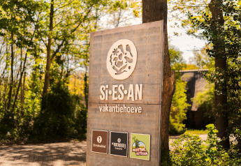 Træskilt ved indgangen til Si-Es-An glamping og feriepark, omgivet af grønt og skovklædt område.