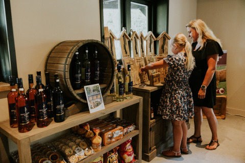 Moeder en dochter bekijken streekproducten in een boerderijwinkel bij een glampingverblijf, vol lekkernijen.