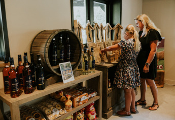 Mor og datter udforsker lokale varer i en butik på glamping-gård, omgivet af mad og drikke.