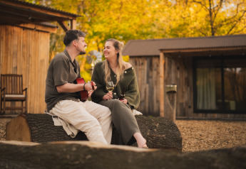 Coppia seduta su un tronco alla casa nella natura «Barn» al campeggio Si-Es-An nei Paesi Bassi, con chitarra e vino.