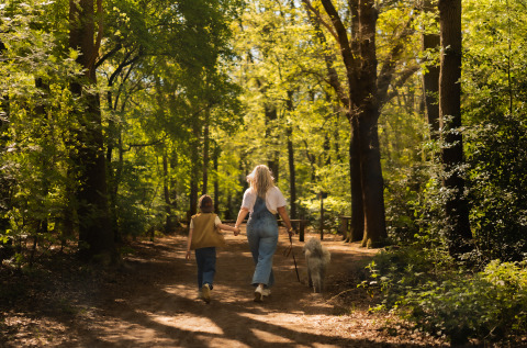Mother and daughter walking their dog along a scenic forest trail near their glamping accommodation.