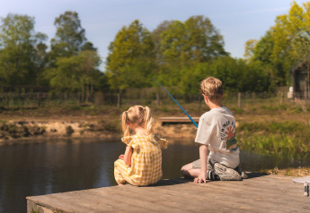 Dos niños sentados en un muelle de madera pescando junto a un lago en un entorno natural de glamping.