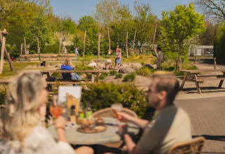 Buiten glamping accommodatie met volwassenen aan tafel en spelende kinderen in de achtergrond.
