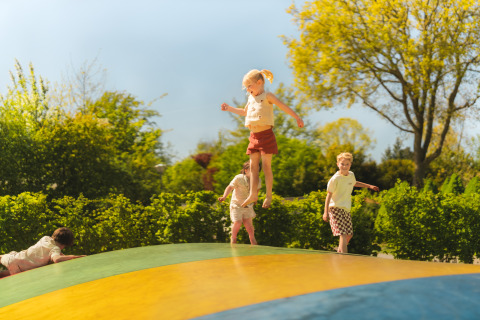 Kinder spielen und springen auf einem großen aufblasbaren Kissen draußen bei einem Glampingplatz im Grünen.