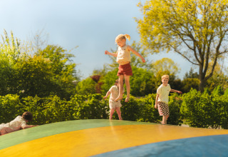 Children jumping and playing on a large outdoor bouncy pillow at a glamping site with trees in the background.