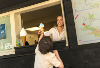 Ein Kind erhält eine Eiswaffel von einer freundlichen Verkäuferin am Fenster einer Glamping-Unterkunft.