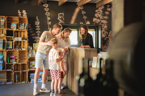 Familie checkt an einer Rezeption mit Naturdekor für einen Glamping-Urlaub ein und lächelt.