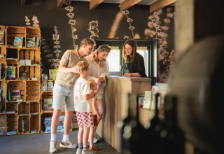 Familie checkt an einer Rezeption mit Naturdekor für einen Glamping-Urlaub ein und lächelt.
