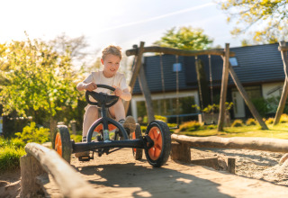 Boy riding a pedal go-kart on a playground at a glamping site, sunshine and cabin in the background.