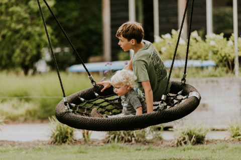 Zwei Kinder schaukeln zusammen auf einer Netzschaukel an einem glamping Platz im Grünen.
