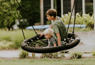 Two children play together on a large net swing in an outdoor glamping setting surrounded by greenery.