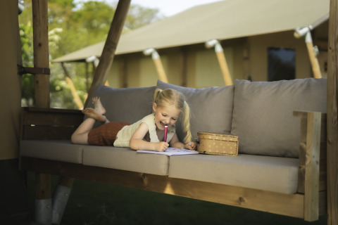 Une fillette dessine et sourit sur un canapé dans une tente safari au camping Si-Es-An, aux Pays-Bas.