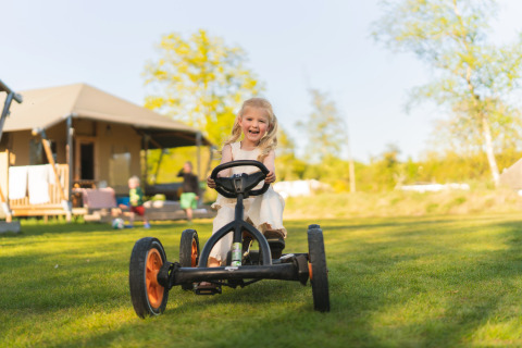 Mädchen fährt fröhlich Gokart vor einem Safarizelt auf dem Campingplatz Si-Es-An in den Niederlanden.