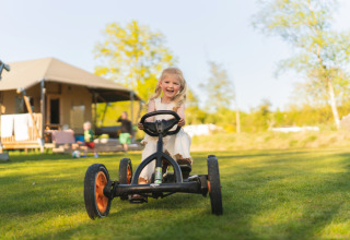 Fille heureuse sur un kart devant une tente safari au camping Si-Es-An, Pays-Bas, journée ensoleillée.