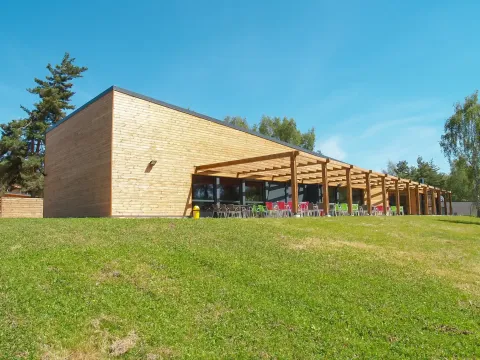 Modernes Holzgebäude mit Terrasse und bunten Stühlen im Camping Holiday Park Les Demeures du Lac in Frankreich.