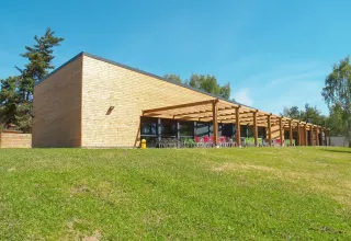 Modern houten gebouw met grote ramen en terrasstoelen op Camping Holiday Park Les Demeures du Lac, Frankrijk.
