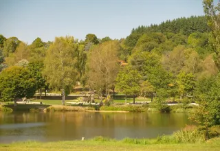 Vista de un lago tranquilo con árboles verdes y área de juegos cerca de Saint-Rémy-sur-Durolle, Francia.
