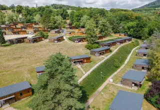 Feriepark med træhytter omgivet af grønne bakker og træer i Auvergne-Rhône-Alpes, Frankrig.
