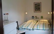 Lichte slaapkamer met dubbel bed, geruit beddengoed en muurkunst in lodge Am Strand in Duitsland.
