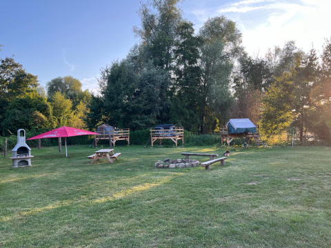 Glamping site featuring raised tent platforms, a central fire pit, and picnic tables at Dachzelt Dorf Sandstedt.