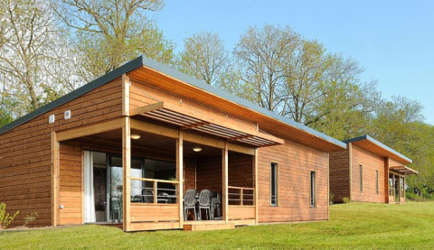 Cabañas de madera en una lodge, con terrazas cubiertas, sillas de jardín y césped verde entre árboles.