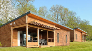Moderne Holzhütten einer Lodge mit Terrasse, Rasenfläche und Bäumen an einem sonnigen Tag.