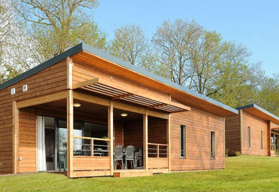 Moderne Holzhütten einer Lodge mit Terrasse, Rasenfläche und Bäumen an einem sonnigen Tag.