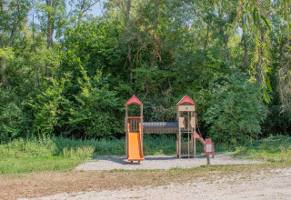 Spielplatz im Ferienpark mit Rutsche und Spielturm, umgeben von Bäumen, perfekt für Glamping.