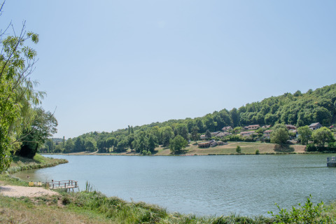 Vue sur un lac avec forêt et parc de vacances proposant du glamping sous un ciel bleu clair.