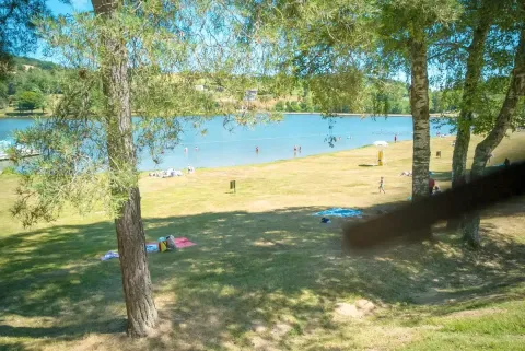 Lago con personas nadando y descansando sobre el césped en Camping Paradis Les Chanterelles, Auvernia-Ródano-Alpes, Francia.