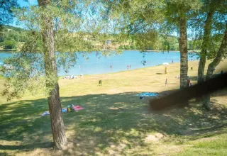 Lago con personas nadando y descansando sobre el césped en Camping Paradis Les Chanterelles, Auvernia-Ródano-Alpes, Francia.