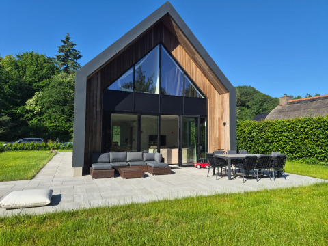Moderne lodge genaamd Forest villa Zoethout met grote ramen, buitenzitjes en groene tuin.
