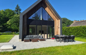 Moderne lodge met de naam Forest villa Zoethout, grote ramen, buitenzitjes en groene tuin.