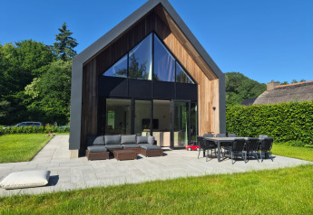 Lodge moderno llamado Forest villa Zoethout con grandes ventanales, zona de estar exterior y jardín verde.