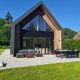 Modern lodge named Forest villa Zoethout with large windows, outdoor seating, and a lush green garden.