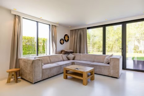 Moderne woonkamer in Forest villa «Zoethout» in De Kremmer, Nederland, met hoekbank en uitzicht op tuin.