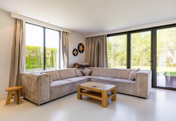 Sala moderna de Forest villa «Zoethout» en De Kremmer, Países Bajos, con sofá esquinero y ventanales al jardín.