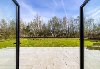 Uitzicht door open glazen deuren naar terras en tuin bij Forest villa «Zoethout» in De Kremmer, Nederland.