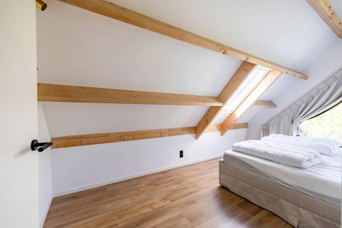 Lichte slaapkamer met houten balken in Forest villa «Zoethout» te De Kremmer, Nederland met dakraam.