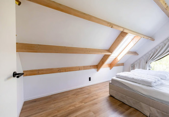 Dormitorio abuhardillado en Forest villa «Zoethout» en De Kremmer, Países Bajos, con vigas y claraboya.