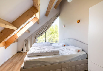 Camera da letto luminosa con arredo moderno, grandi finestre e travi a vista nella Forest villa Zoethout.