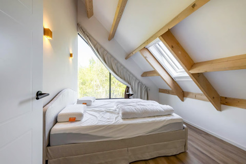 Slaapkamer met houten balken en groot raam in Forest villa «Zoethout» bij De Kremmer, Nederland.