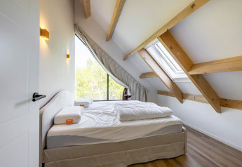 Dormitorio con vigas de madera expuestas y gran ventanal en la Forest villa «Zoethout» en De Kremmer, Países Bajos.