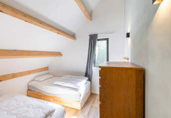 Habitación luminosa con dos camas individuales y cómoda de madera en la Forest villa «Zoethout», De Kremmer.