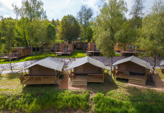 Tentes safari et cabanes en bois entourées de verdure, parfaites pour un séjour de glamping reposant.
