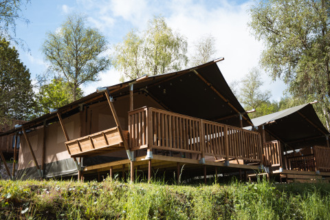 Tente safari avec terrasse en bois au Hameau de l'Ourthe en Belgique, entourée de nature sous le soleil.