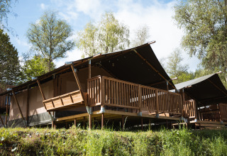 Tente safari avec terrasse en bois au Hameau de l'Ourthe en Belgique, entourée de nature sous le soleil.