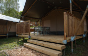 Safaritent met houten terras en stoelen bij Hameau de l'Ourthe in België, tussen het groen gelegen.